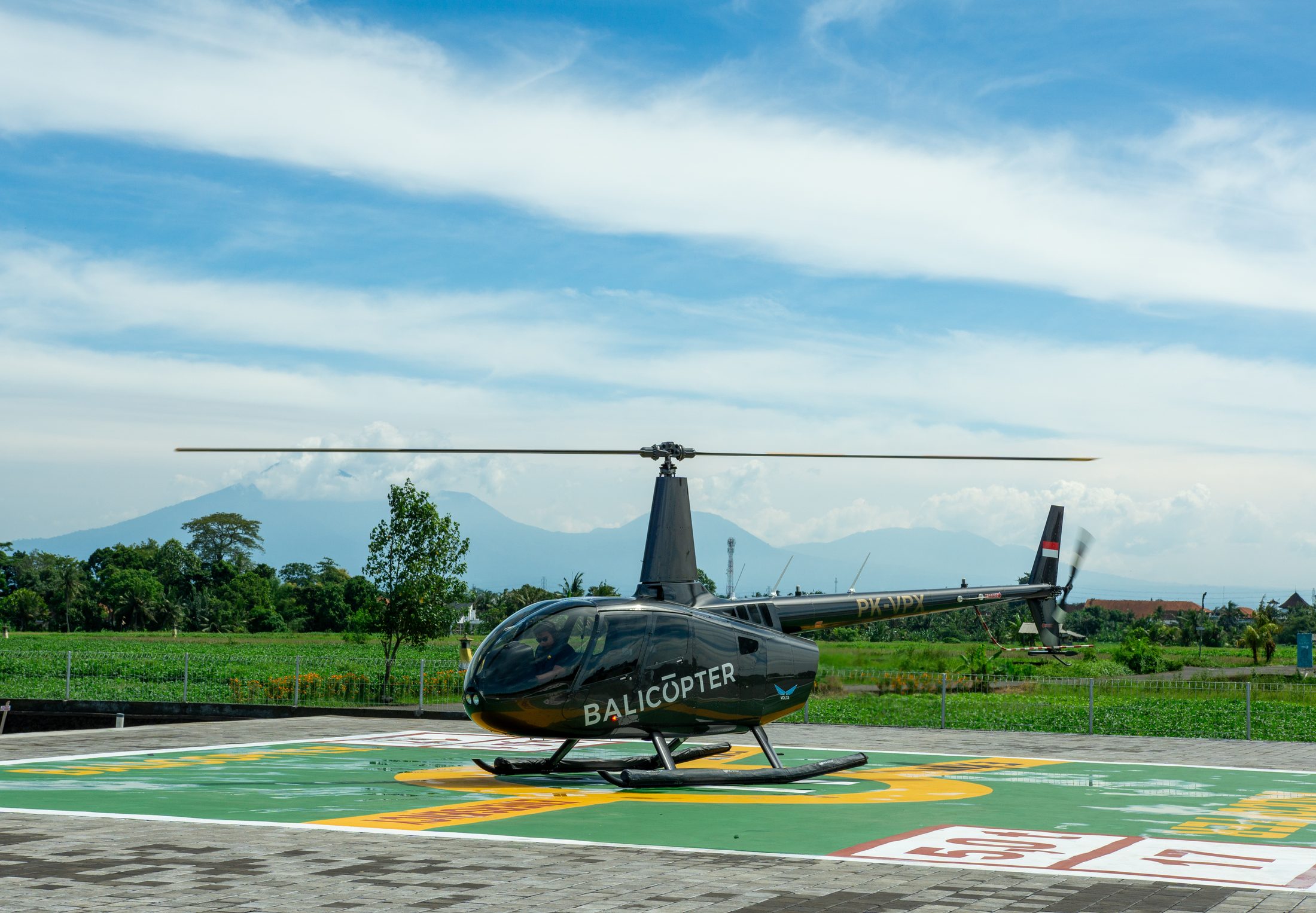 Four-seat turbine helicopter on the marked pad at the Nuanu heliport, rice fields and mountains beyond
